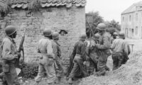 [ORIGINAL CAPTION] ALLIED INVASION OF FRANCE... A platoon of Negro troops surrounds a farm house in a town in France, as they prepare to eliminate a German sniper holding up an advance. 10 June 1944. Omaha Beachhead, near Vierville Sur-Mer, France